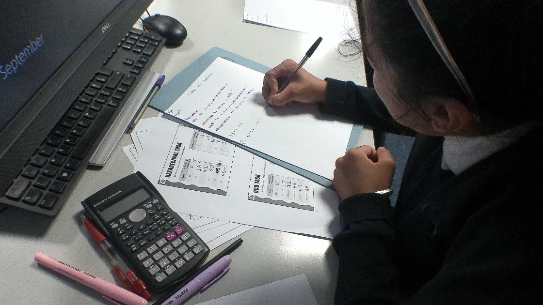 Student working on a computing assignment with a calculator and computer