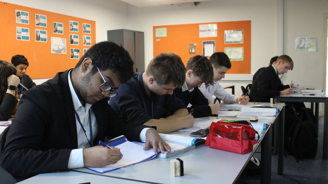 Students in a classroom focused on writing during a maths lesson