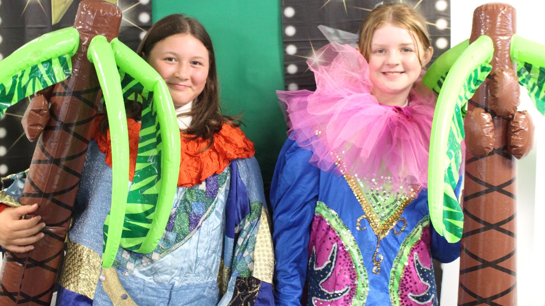 Two students in colourful costumes holding inflatable palm trees