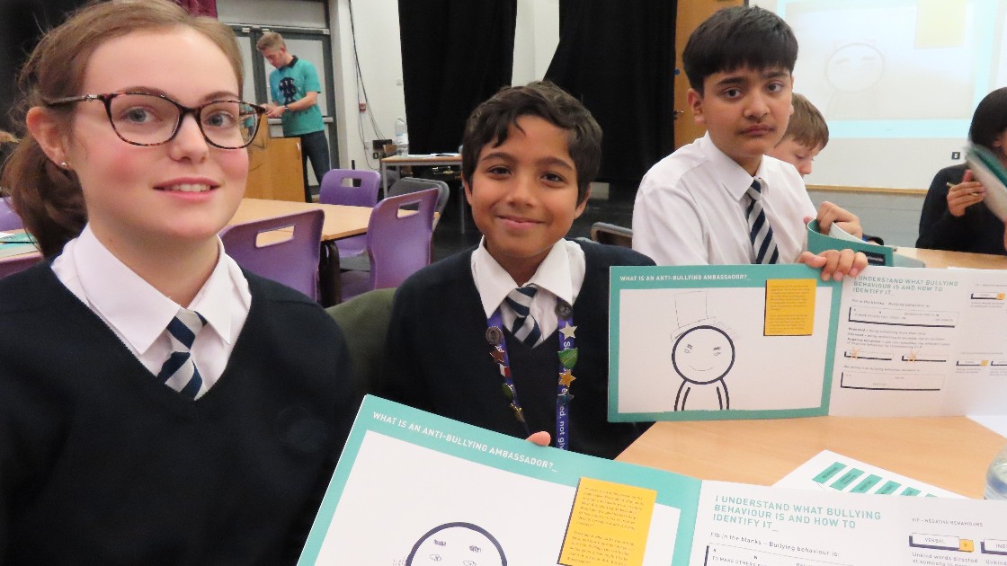 Students at an anti-bullying trip showing ambassador worksheets at a workshop table