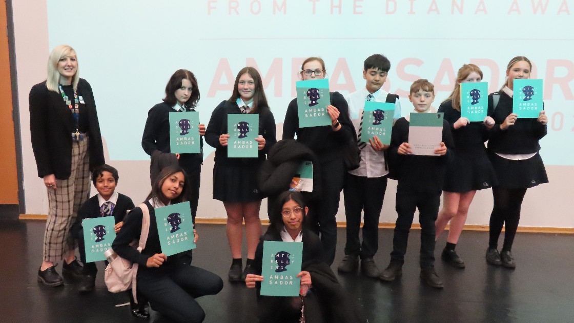 Students holding Anti-Bullying Ambassador certificates on stage with a teacher