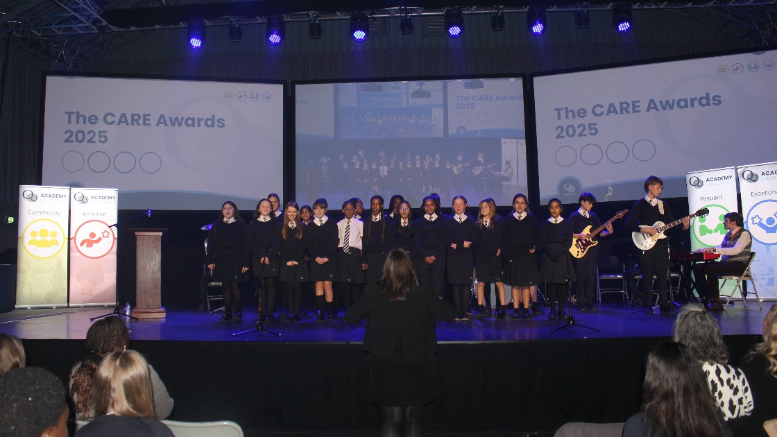 Students performing on stage at the CARE Awards assembly with a teacher conducting