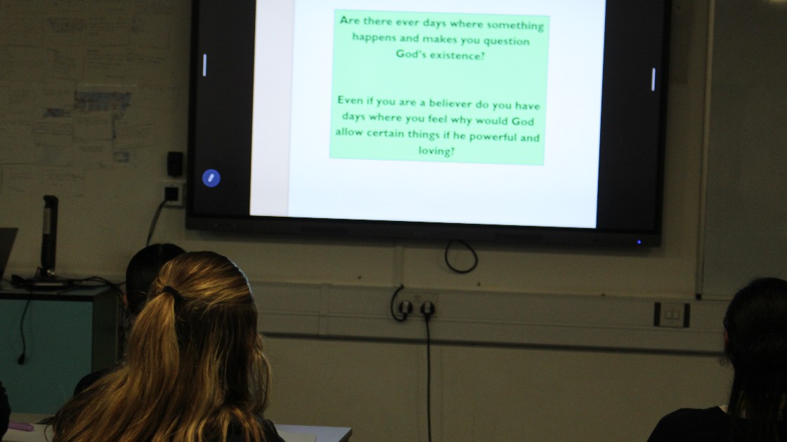 Students in an RS lesson viewing a slide with questions about God’s existence on the classroom screen